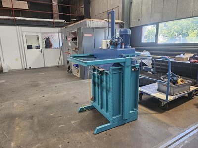 Seitenansicht einer blauen Ballenpresse Austro K65 mit ausgeklappter Einfüllrutsche, in einer Werkhalle zwischen Werkstattausrüstung.