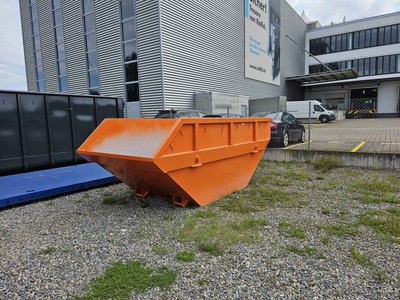Stapelbare, offene 10 m³-Absetzmulde (Sperrgutmulde) in Orange, stehend auf Kiesfläche vor einem Büro-/Industriegebäude.