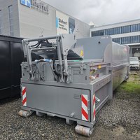 brollpresscontainer der Marke Beringer mit Hebekippvorrichtung (HKV) in Grau RAL 9006 auf Lagerplatz vor Firmengebäude – effiziente Lösung für industrielle Abfallverdichtung.