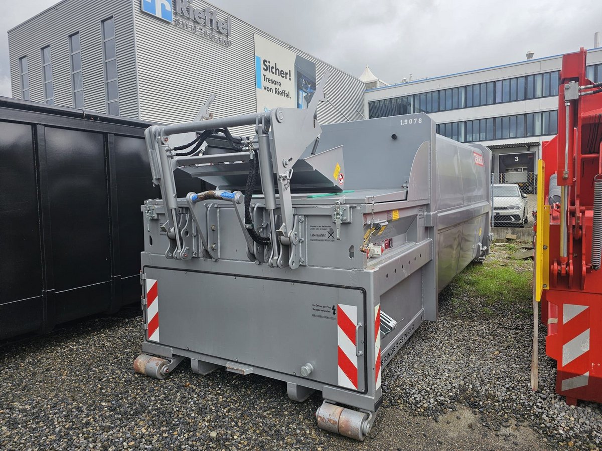 brollpresscontainer der Marke Beringer mit Hebekippvorrichtung (HKV) in Grau RAL 9006 auf Lagerplatz vor Firmengebäude – effiziente Lösung für industrielle Abfallverdichtung.