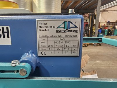 Nahaufnahme des Typenschilds der blauen Ballenpresse Austro K65 mit Hersteller-, Seriennummer- und Leistungsangaben (Baujahr 2023, Presskraft 50 kN, Motor 1,5 kW / 230 V).