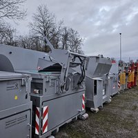 Mehrere Abrollpresscontainer der Marke Beringer in Grau RAL 9006 auf Lagerplatz – Varianten ohne Aufbau, mit Hebekippvorrichtung (HKV) und mit Einfülltrichter im direkten Vergleich.